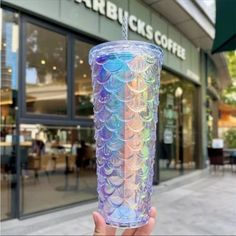 a person holding up a plastic cup in front of a starbucks coffee shop that has holographics on it