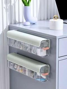 two clear plastic drawers on top of a white desk next to a vase with flowers