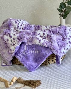 a purple and white blanket sitting on top of a bed next to a wooden bead necklace