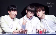 three young men sitting next to each other at a table with an electronic device in front of them