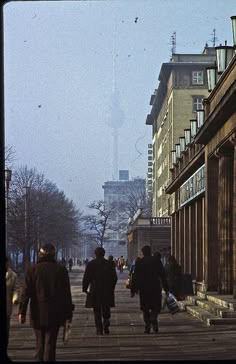 several people walking down the street in front of tall buildings on a foggy day