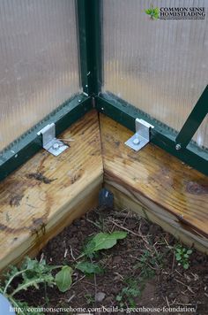 the corner of a garden shed with two metal brackets on it's sides and plants growing in the ground below