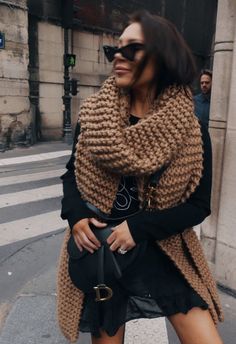 a woman is walking down the street with her hand in her pocket and wearing a scarf around her neck