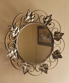 a round mirror hanging on the wall above a table with a vase and flowers in it