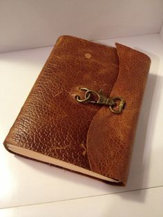 a brown leather book with a key on the front and inside cover is sitting on a white surface