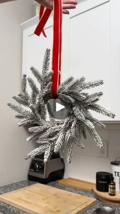 a person holding a red ribbon over a christmas wreath on top of a kitchen counter