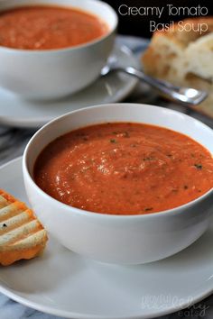 a white plate topped with a bowl of tomato soup next to a slice of bread