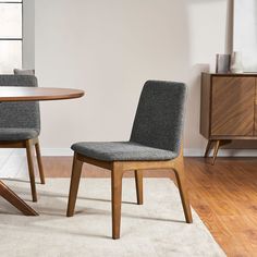 two gray chairs sitting next to each other on top of a white rug in front of a wooden table