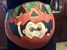 a pregnant woman with her belly painted to look like a cartoon character holding a pumpkin