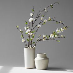 two white vases with flowers in them sitting on a table next to each other