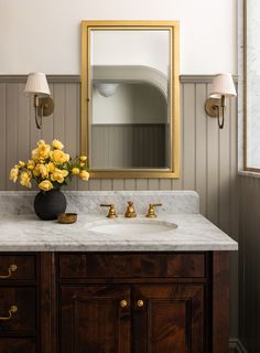 a bathroom vanity with marble counter top and gold framed mirror above it, along with yellow flowers