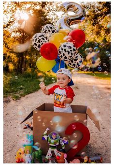 a little boy is sitting in a box with balloons and other toys on the ground