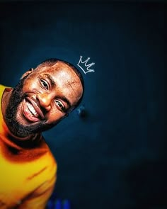 a man with a crown on his head smiles at the camera while wearing a yellow shirt