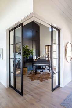 an open door leading to a living room with a piano on the floor and a potted plant