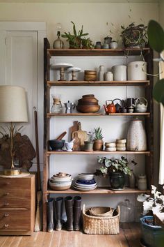 a shelf filled with pots and pans next to a lamp on top of a wooden floor