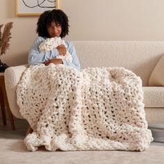 a woman sitting on a couch holding a crocheted blanket