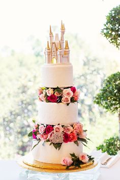 a three tiered wedding cake with flowers on the side and a castle topper