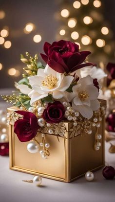 a gold box with red and white flowers in it sitting on a table next to pearls