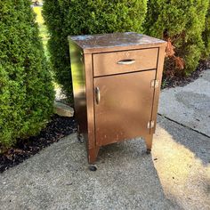 an old metal cabinet sitting in the middle of a sidewalk next to some shrubbery