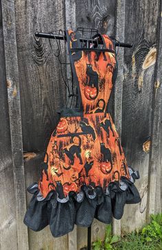 an orange and black dress with cats on it is hanging from a wooden fence outside