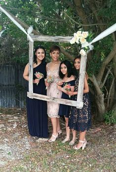 four women pose for a photo in front of a wooden frame with flowers on it