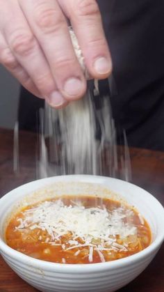 a person sprinkling parmesan cheese on top of a bowl of soup