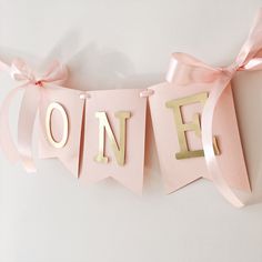 a pink banner with the word one hanging from it's side and ribbon on top