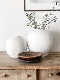 two white vases sitting on top of a wooden dresser next to a plant in a vase