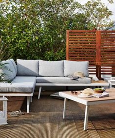 a couch and coffee table on a wooden deck in the middle of a garden area