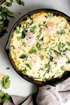 baked eggs with herbs in a skillet on a white countertop next to bread and parsley