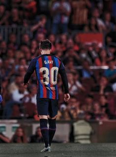 two soccer players are walking in front of an audience at a sporting event, one has his foot on the ground