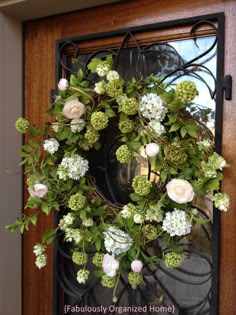 a wreath with white flowers and green leaves hanging on a front door window sill