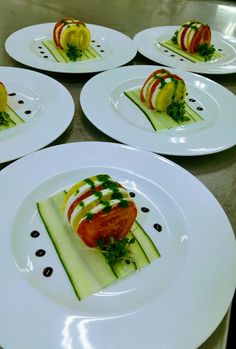 four white plates topped with slices of cucumber and tomato on top of each other