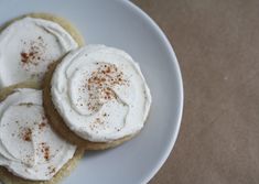 three cookies with white frosting and cinnamon sprinkles on top sit on a plate