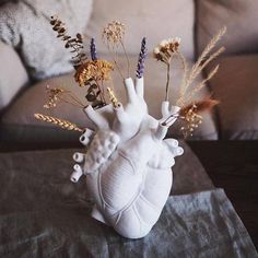 a heart shaped vase with dried flowers in it on a table next to a couch