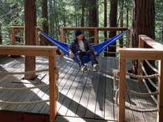 a man sitting in a hammock on a wooden deck surrounded by tall trees