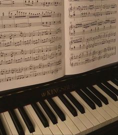 an open book with sheet music on it and piano keys in the foreground,