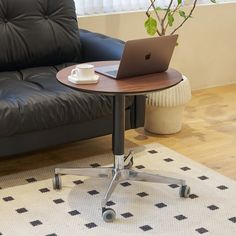 a laptop computer sitting on top of a wooden table next to a black leather couch