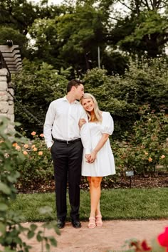 a man and woman standing next to each other in front of some bushes with flowers