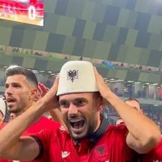 two men in red shirts and white hats are holding their hands up to their ears