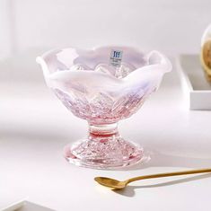 a glass bowl sitting on top of a table next to a gold spoon and bottle