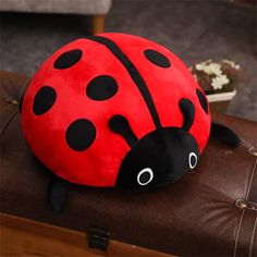 a stuffed ladybug sitting on top of a brown suitcase