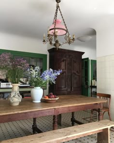 a wooden table topped with vases filled with flowers next to a light fixture hanging from the ceiling