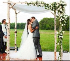 a bride and groom kissing under an arch with flowers on the altar at their wedding