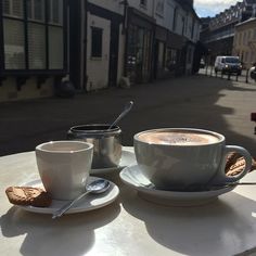 two cups of coffee sitting on top of a table next to each other in front of buildings