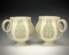 two white vases sitting next to each other on a gray surface with black background