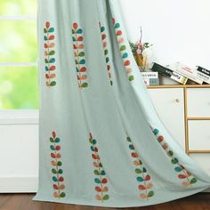 a curtain with colorful leaves on it in front of a white wall and wooden floor