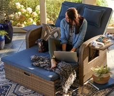 a woman sitting in a chair with a laptop on her lap and a dog laying next to her