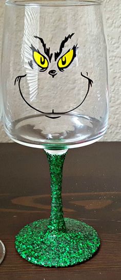 a wine glass with a face drawn on the side and green glitter in front of it