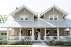 a bride and groom standing in front of a large gray house with white porches